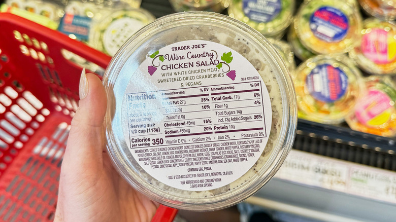 A hand holding a container of chicken salad