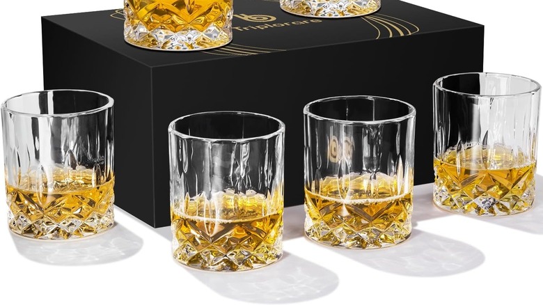 Rocks glasses containing amber liquid arranged around a gift box.