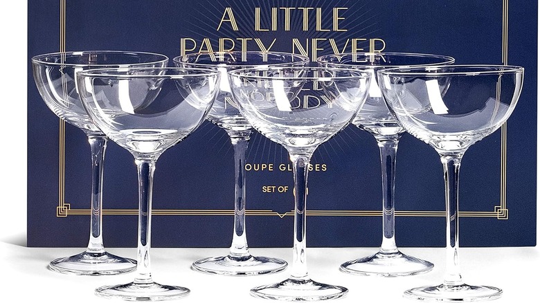 A set of six coupe glasses in front of a blue gift box.