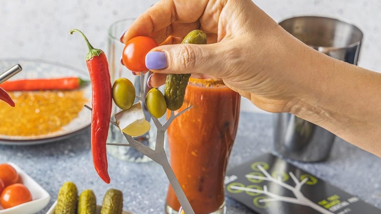 Hand placing peppers, tomatoes, olives, and pickles on a bloody Mary branch