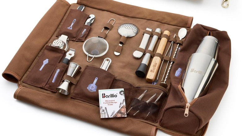 A traveling bar kit rolled out to reveal tools like a cocktail shaker, spoon, and strainer.