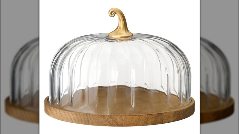 A pumpkin-shaped glass dome with a golden stem on top of a wooden base.