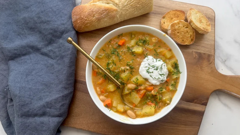 A bowl of Creamy Dill Pickle Soup with a toasted baguette on a cutting boar