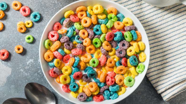 Bowl of Froot Loops next to a gray and white striped dish towel on a gray stone surface