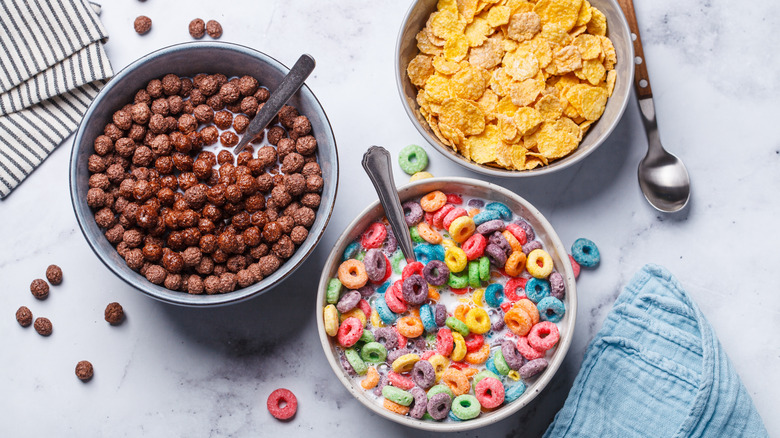 Assorted bowls of cereal with different spoons and cloth napkins on a white marble surface