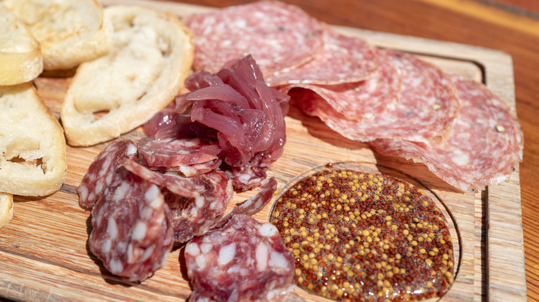 Italian cold cuts sitting on a charcuterie tray with mini toasts and other foods