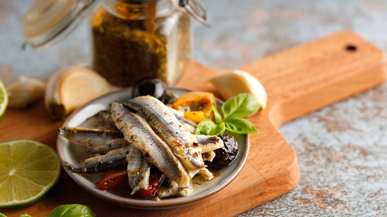 Whole anchovies with roasted vegetables on a small plate in front of an open jar of anchovy paste