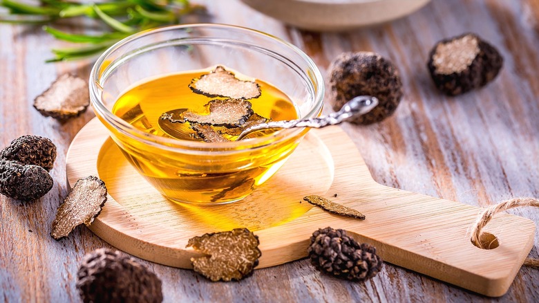 Gold-colored oil with dried black truffles in a small clear bowl on a wooden serving board