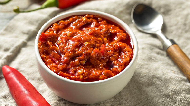 Calabrian chili paste in a small white bowl next to a metal spoon with a wooden handle