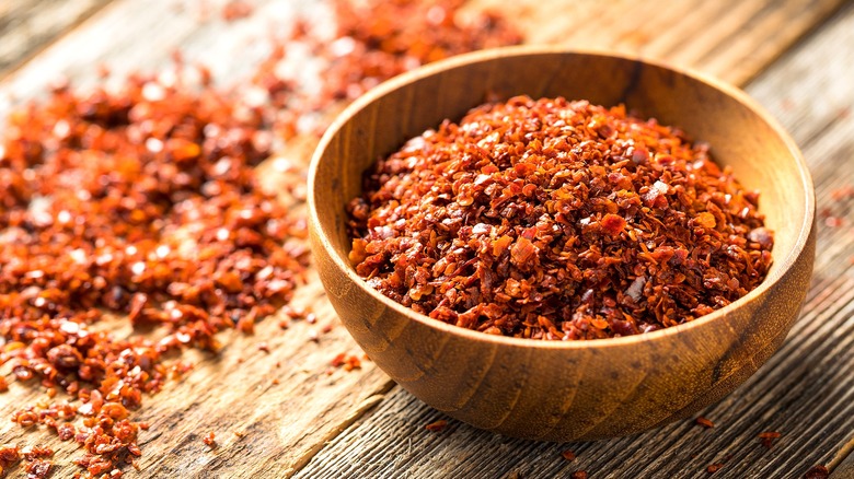 Crushed red pepper flakes in a small wooden bowl on a wood surface