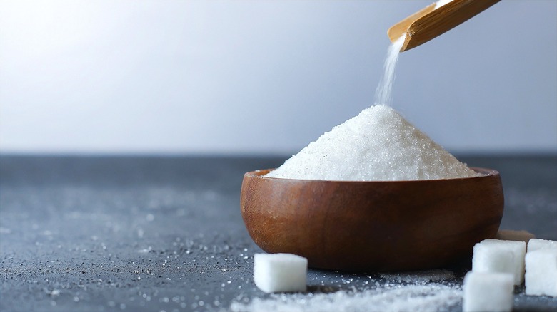Granulated sugar in a small wooden bowl surrounded by sugar cubes