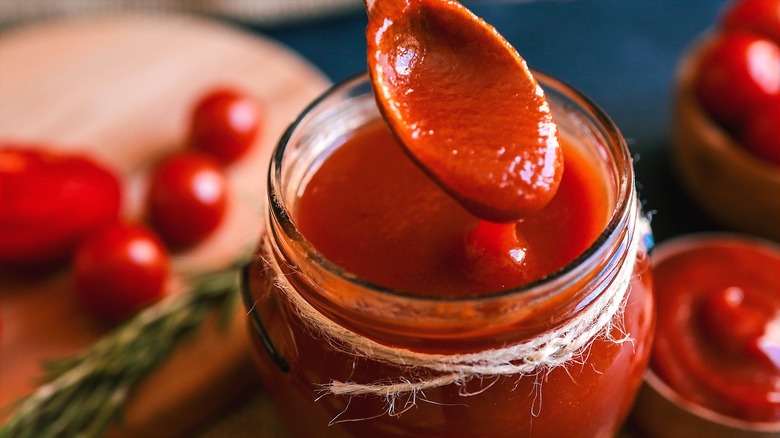 A spoon in an open jar of red tomato sauce with twine around the rim