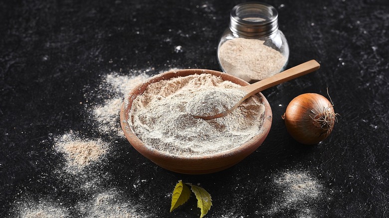 Onion powder in a small wooden bowl with a wooden spoon and in a small glass jar on a black surface