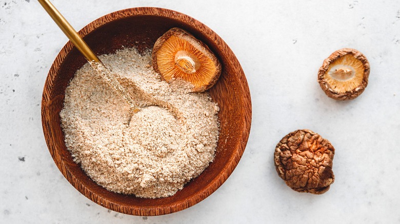 Top-down view of dried mushroom powder with whole dried mushrooms in a wooden bowl with a gold spoon