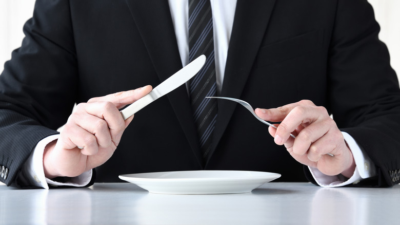 Businessman holding a fork and knife with his elbows off the table