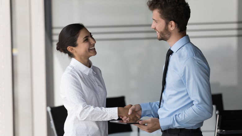 Man standing greeting a woman and shake her hand