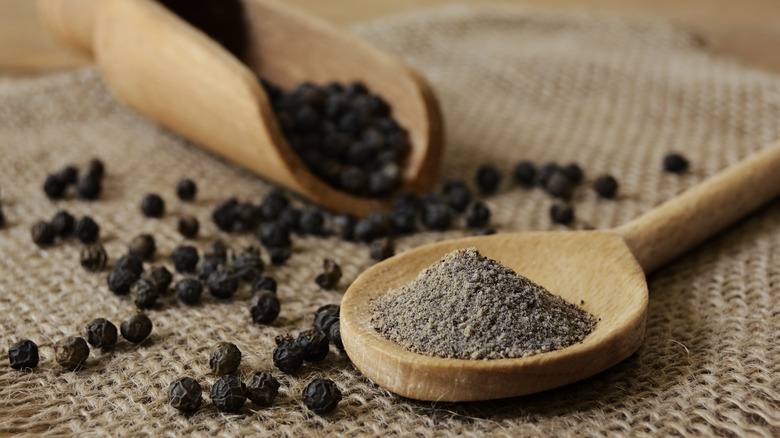 Wooden spoons of ground and whole black peppercorns on burlap