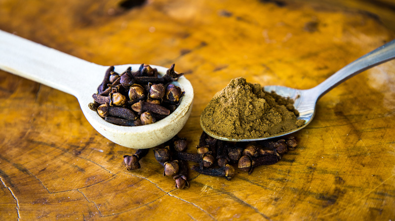 Wooden spoon of whole cloves and metal spoon of ground cloves