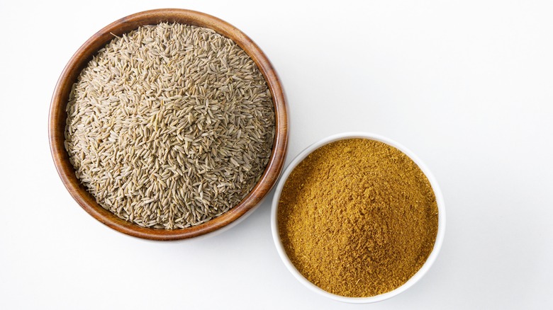 Two wooden bowls filled with cumin seeds and ground cumin