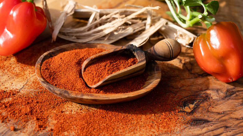 Wooden scooper and bowl filled with paprika surrounded by fresh red peppers