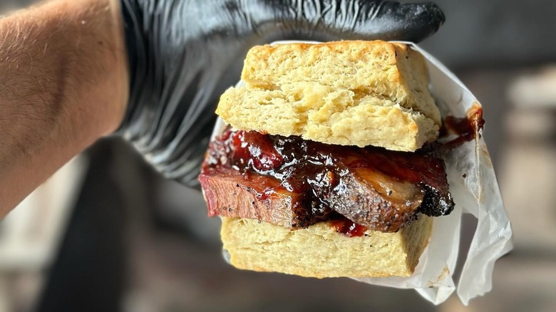 A person holding a barbecue beef biscuit sandwich