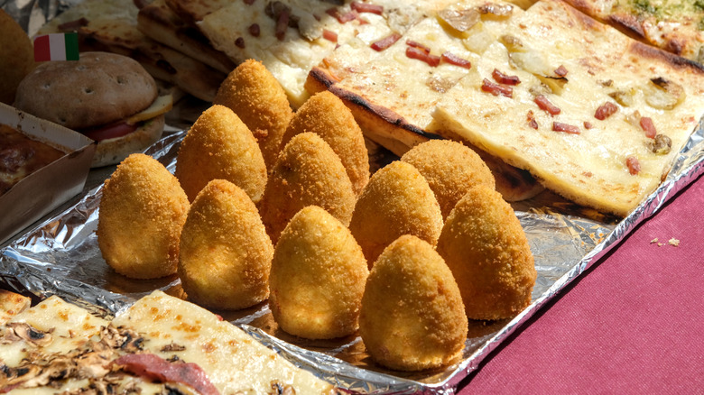 A tray of arancini next to focaccia on a foil tray