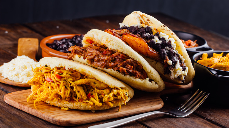 Three arepas on a wooden cutting board stuffed with meat, beans, and cheese.