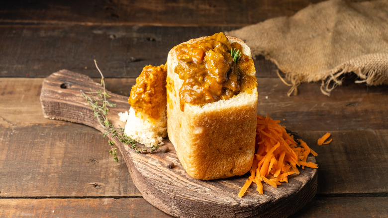 South African bunny chow on a wooden cutting board with grated carrot