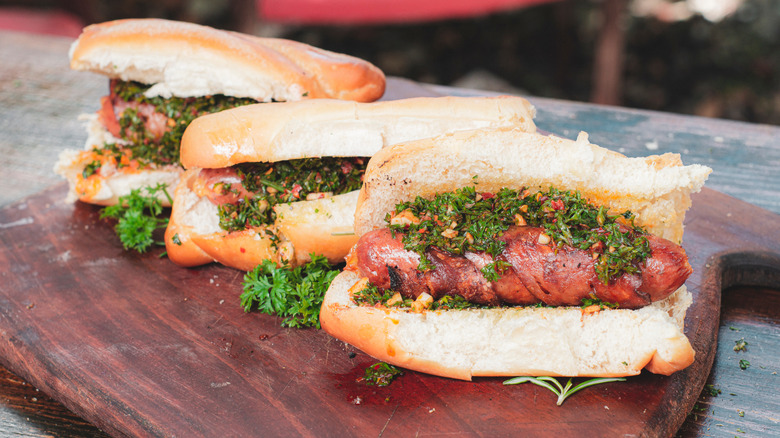 Three choripán sandwiches on a wooden cutting board