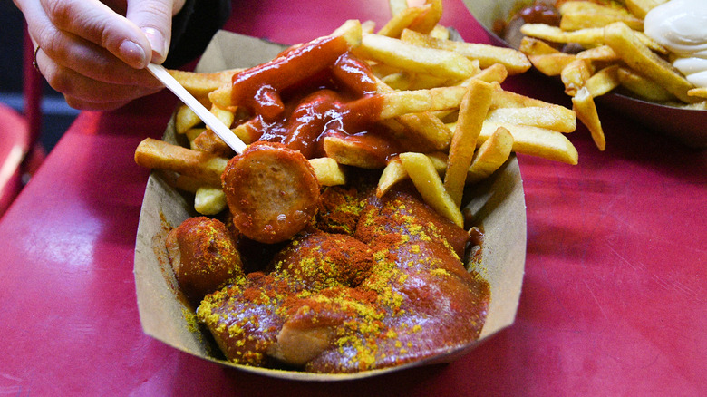 A person eating currywurst with fries