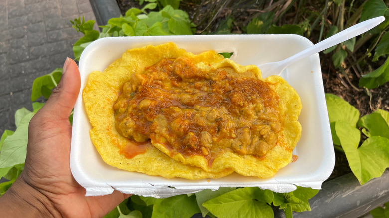 A person holding a styrofoam plate of doubles
