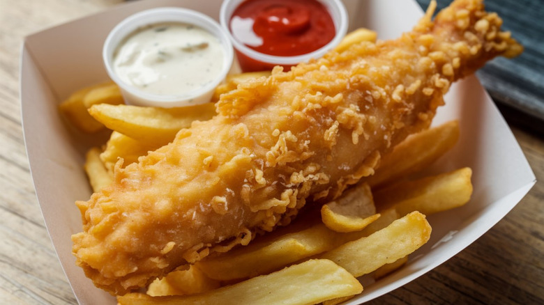 A carton of fish and chips with ketchup and tartar sauce