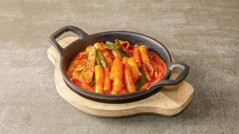 A cast iron dish of tteokbokki on a wooden holder