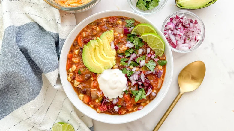 A bowl of Basic 3-Bean Vegetarian Chili with a kitchen towel and spoon beside it