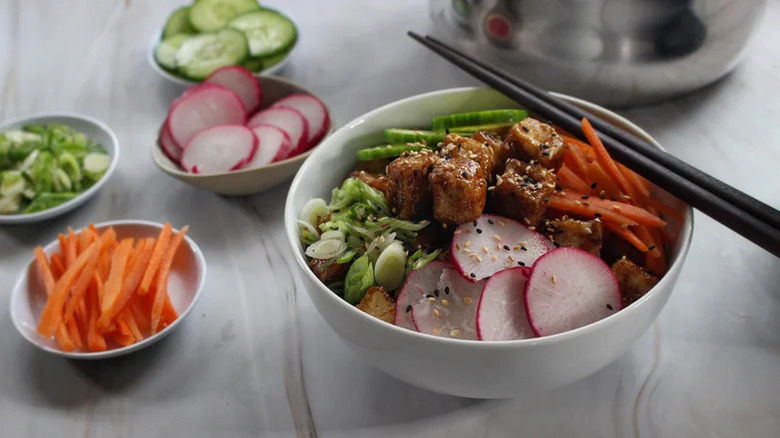 A Crispy Ginger-Glazed Tofu Bowl with dished ingredients behind it
