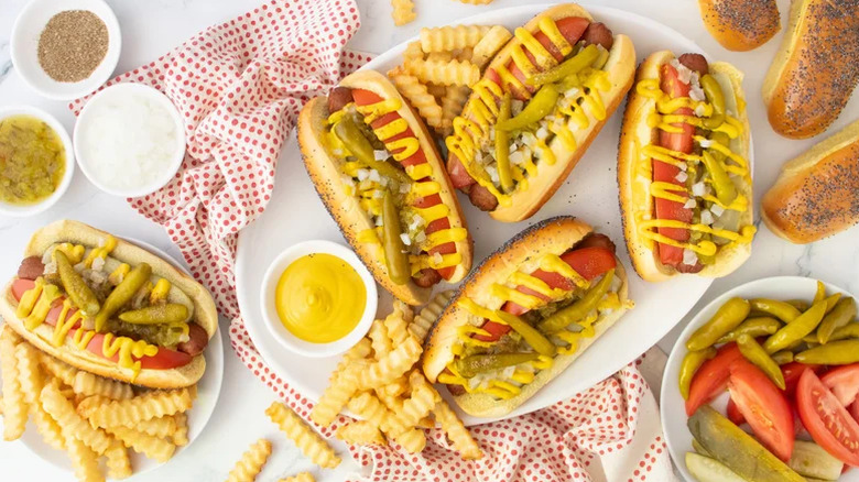 Chicago-Style hot dogs served beside a bow of tomatoes, pickles, and sports peppers as toppings