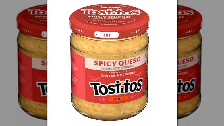 Glass jar of Tostitos spicy queso dip with a red metal lid on a white background.