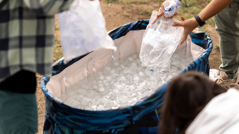 People pouring ice from plastic bags into a cooler.