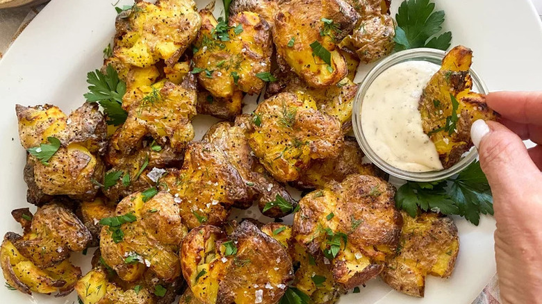 Plate of smashed potatoes with fresh herbs and dipping sauce