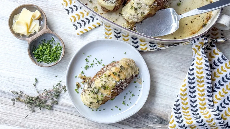 Hasselback potato loaded with cheese and herbs on a plate next to ingredients