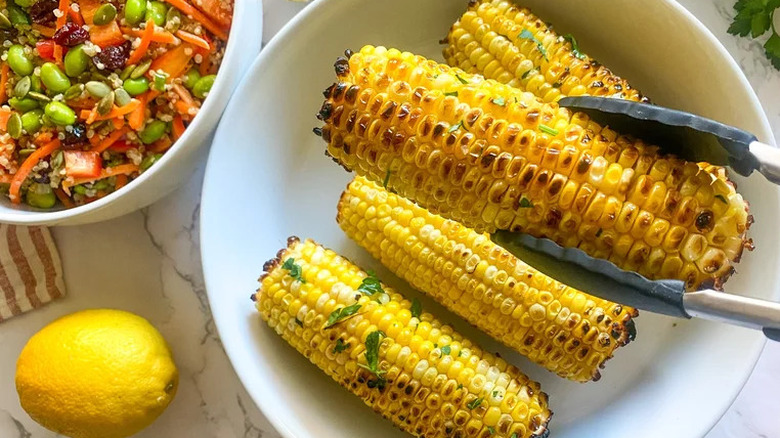 Bowl of corn on the cob with one cob held by tongs