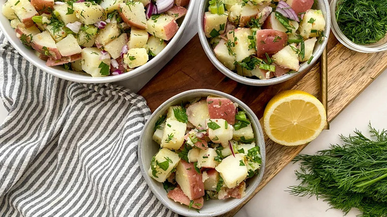 Bowl of potato salad with fresh herbs and ingredients around it