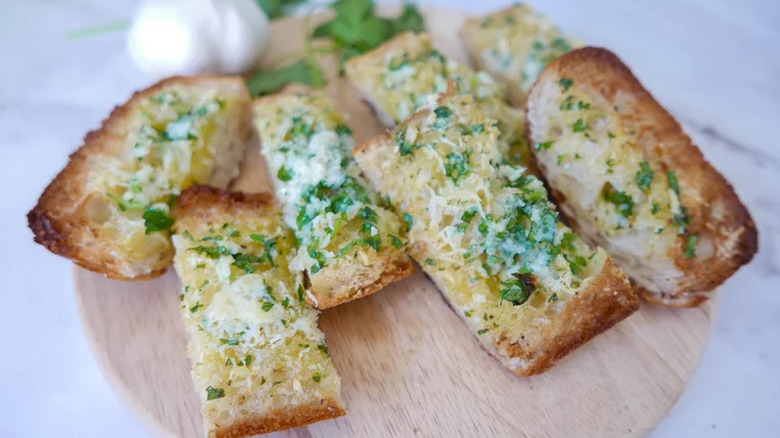 Wooden plate of garlic bread slices with fresh herbs and parmesan