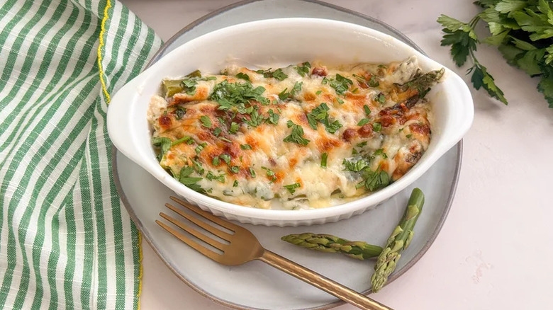 Dish of creamy asparagus casserole with a fork and green and white striped dish towel.