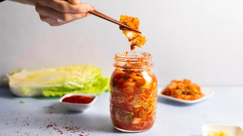 Jar of kimchi with hand and chopsticks.