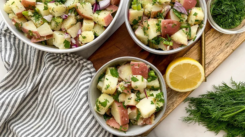 Herbed potato salad in several bowls on a board with dill and citrus.