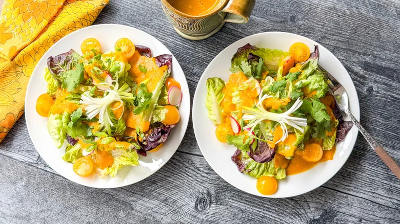 Plates of fresh salad with dressing on a wooden table.