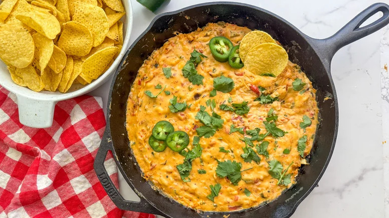 Skillet with queso and corn chips next to a red gingham towel on a marble table.