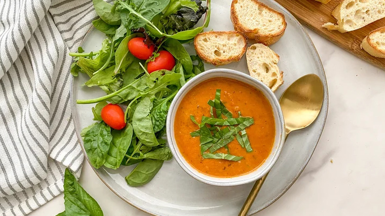 Tomato soup in a bowl with bread and salad