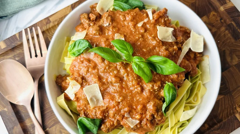 Bolognese over a bowl with pasta and basil